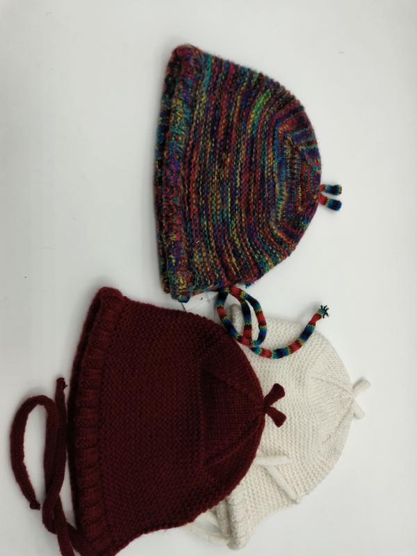 Three handknitted baby bonnets in multicolor variegated, dark red burgundy, and cream white yarn with tie strings
