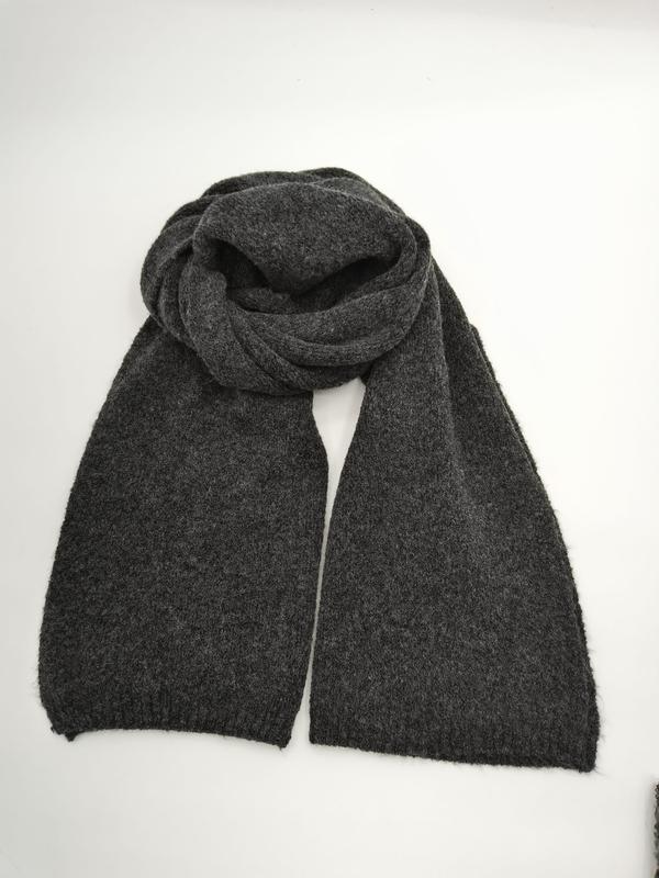 Dark charcoal grey knitted scarf loosely coiled and laid flat on white background showing two long ends