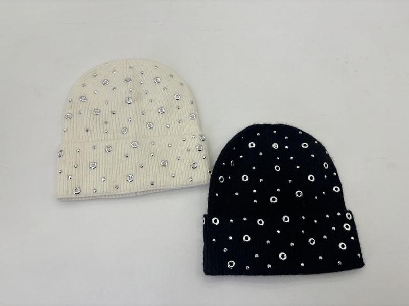 Two knit beanies in cream and black adorned with silver grommet rings and rhinestone studs on a white background