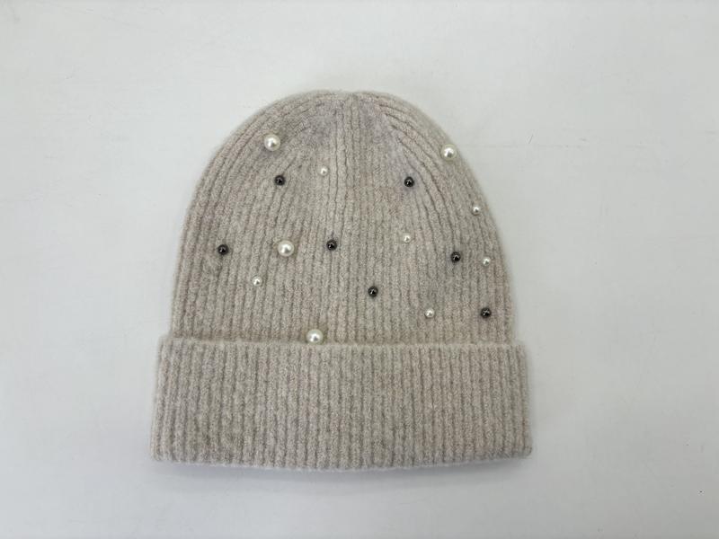 Flat lay of a beige ribbed knit beanie hat decorated with scattered white pearls and dark crystal studs on white background