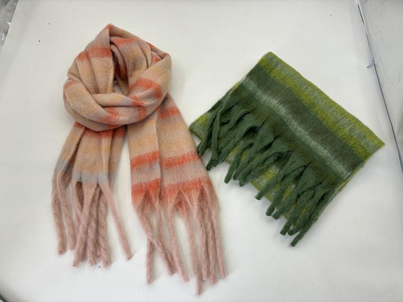 Two plush striped fringe scarves laid flat: one pink and coral, one folded in olive and lime green tones