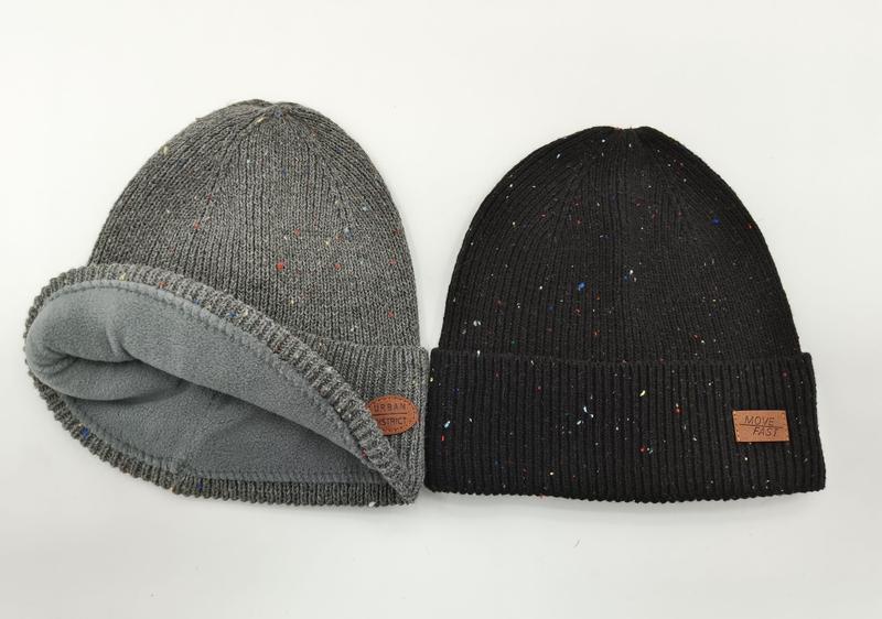 Two speckled knit winter beanies side by side: grey fleece-lined rolled beanie and black ribbed cuffed beanie with leather patch
