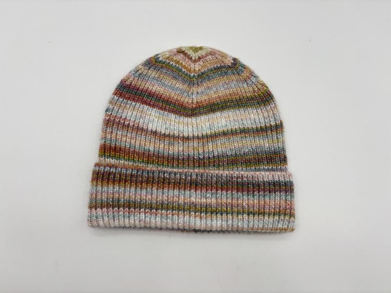 Knitted beanie hat with multicolor space-dyed stripes in pink, green, blue and brown tones, folded cuff, on white background