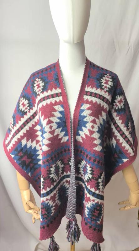Mannequin wearing open-front knit poncho with Aztec geometric pattern in burgundy, blue, white, and black with tassel trim