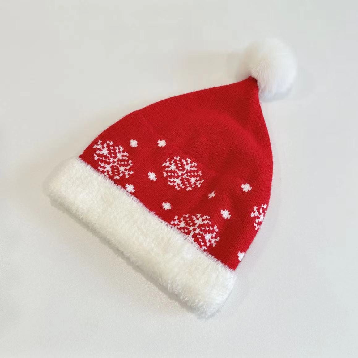 Red knitted Christmas Santa hat with white snowflake pattern, plush white brim, and fluffy pom-pom on white background