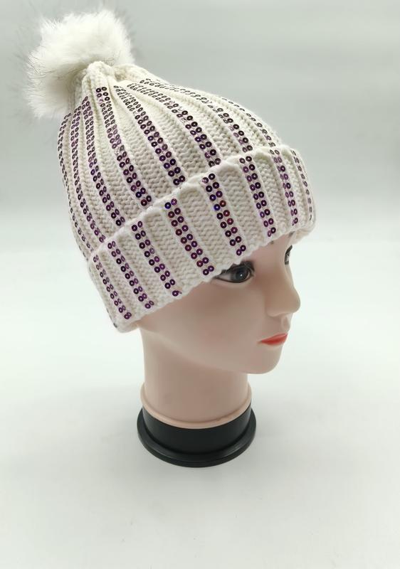White ribbed knit winter beanie with vertical purple sequin stripes and fluffy faux fur pom-pom on mannequin head