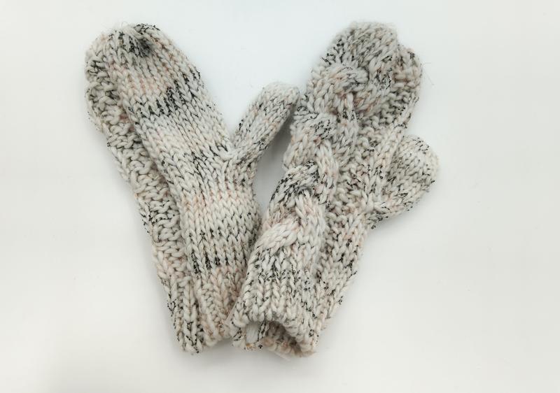 Pair of cream chunky knit mittens with black speckle detail and thumb, laid flat on white background
