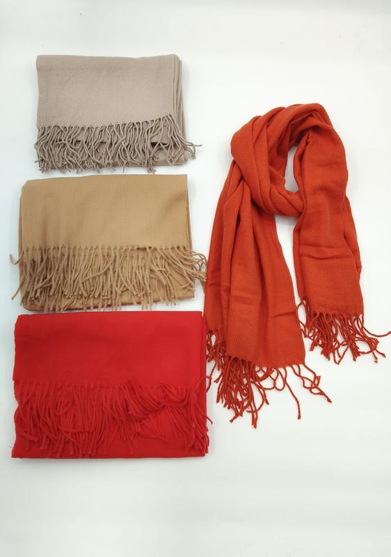 Four solid color pashmina-style scarves with fringe in beige, camel, red, and burnt orange, one draped and three folded
