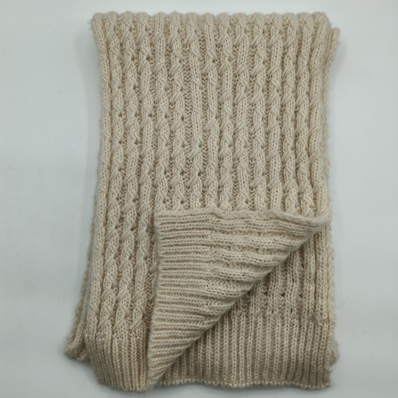 Folded cream chunky cable knit throw blanket with ribbed texture and twisted stitch pattern on white background
