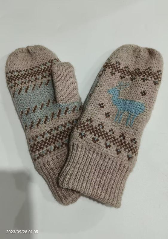 Pair of beige knit winter mittens featuring blue reindeer motif and brown Nordic Fair Isle geometric pattern on white background