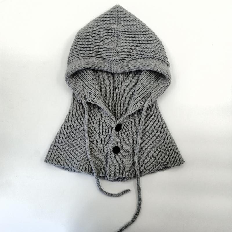 Gray ribbed knit hooded capelet laid flat, featuring two dark buttons, drawstring ties, and a structured hood on white background