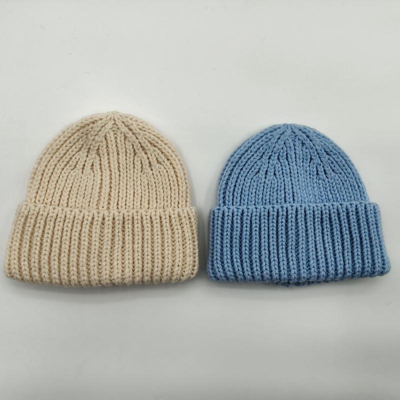 Two chunky ribbed knit beanies laid flat, one in cream and one in sky blue, with folded cuff detail on white background