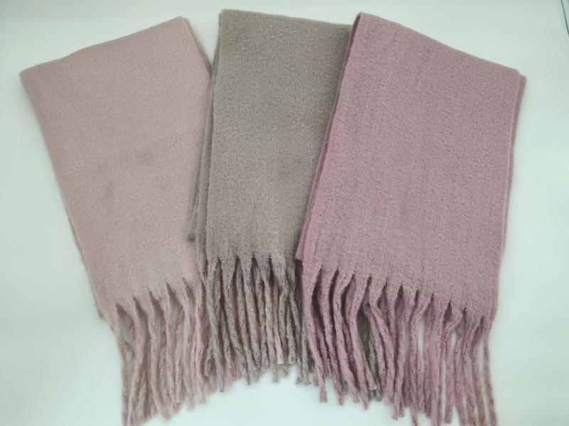 Three folded boucle scarves with fringe ends in blush pink, taupe, and mauve laid flat on white surface