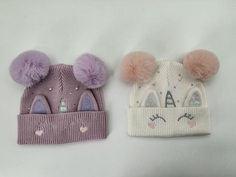 Two unicorn knit beanies in lavender and cream with fluffy double pompoms, glitter horn ears, lash embroidery, and rhinestone details