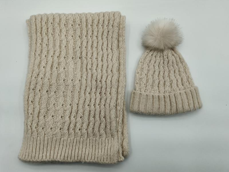 Cream cable knit winter beanie hat with faux fur pom-pom and matching ribbed knit scarf set laid flat