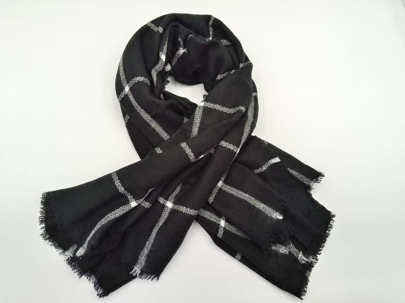 Black woven scarf with white and gray plaid grid pattern, tied in a loose knot, with fringe edges on white background