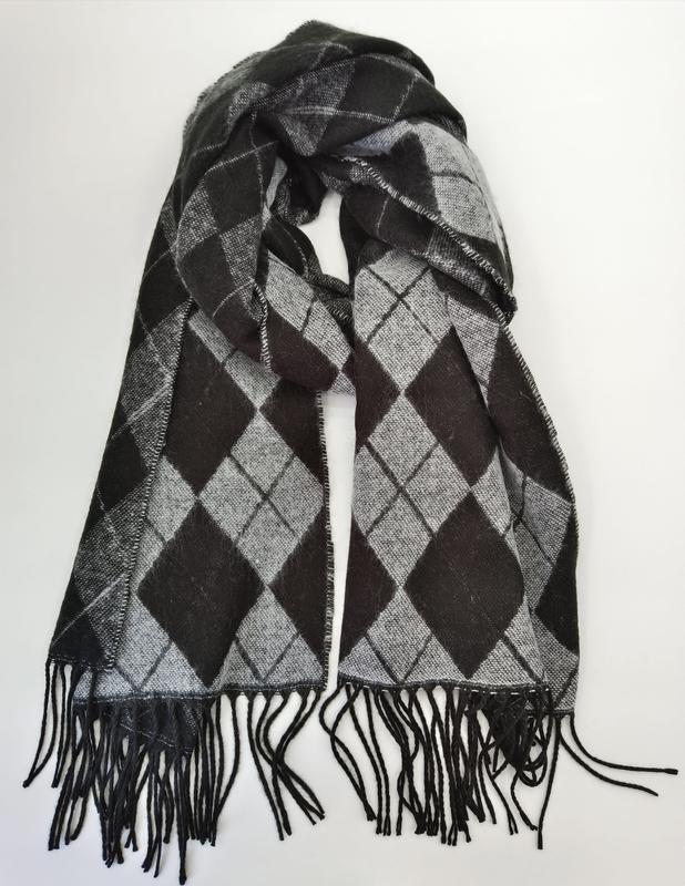 Black and grey argyle diamond pattern woven scarf with black fringe tassels, looped and laid flat on white background
