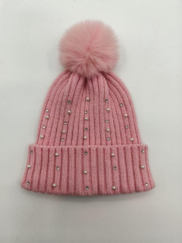 Pink ribbed knit winter beanie hat with faux fur pompom, pearl and crystal rhinestone embellishments on white background