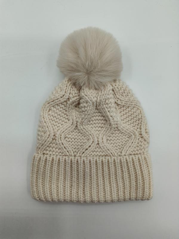 Cream cable knit beanie hat with large fluffy faux fur pom-pom on top and ribbed cuff band