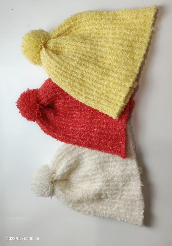 Three stacked chenille knit pom-pom beanies in yellow, red, and white arranged on a white surface