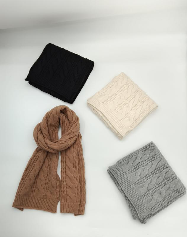 Four cable knit scarves in black, cream, camel, and gray displayed on white background, one unfolded showing full length