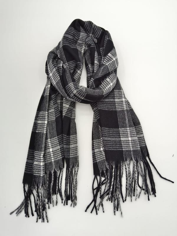 Black and white plaid tartan scarf with fringe ends, loosely knotted and laid flat on white background