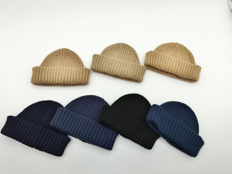Seven ribbed knit cuffed beanie hats in beige, navy, black, and blue tones arranged on white background