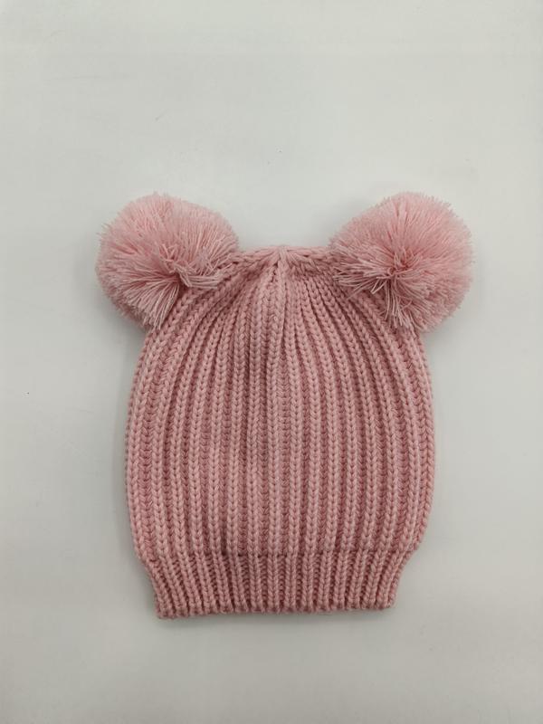 Pink ribbed knit baby beanie hat with two fluffy pom-poms on top, laid flat on white background
