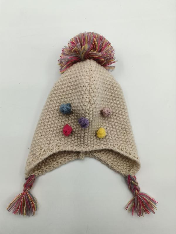 Cream knitted baby earflap hat with large multicolor pompom on top, colorful mini pompom accents, and braided tassel ties