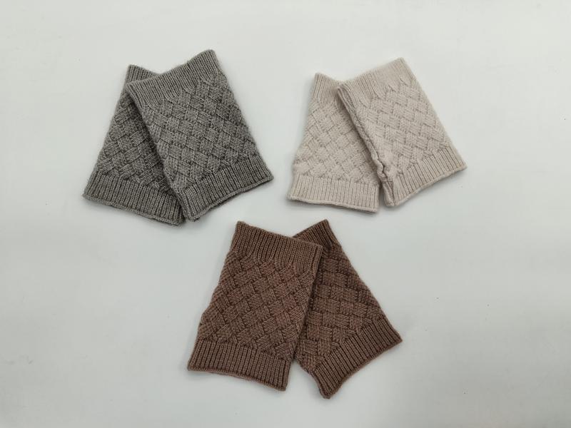 Three pairs of basket weave knit fingerless gloves in grey, cream beige, and brown laid flat on white background