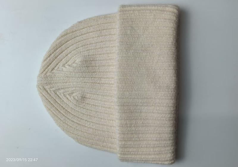 Cream ribbed knit beanie hat laid flat on white surface, showing folded cuff and classic rib stitch texture in natural off-white color