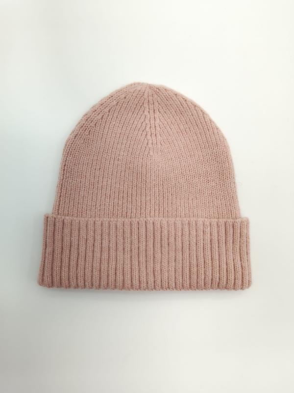 Flat lay of a dusty pink ribbed knit winter beanie hat with a wide folded cuff on a white background