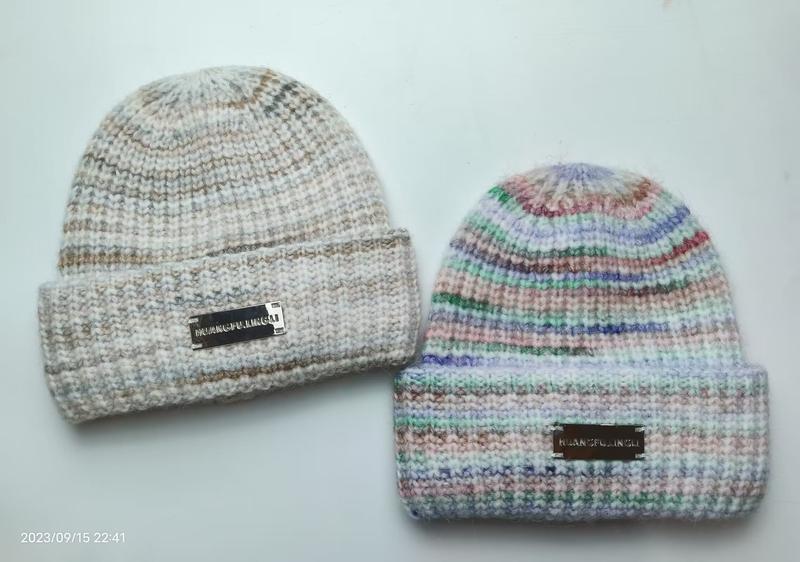 Two chunky knit beanies with folded cuffs: one neutral marled beige, one multicolor pastel striped, both with metal logo labels