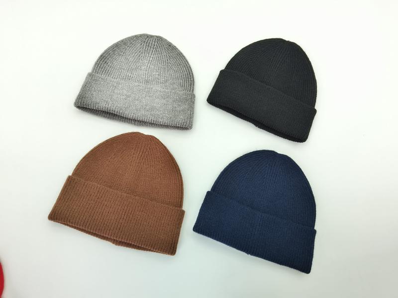 Four ribbed knit cuffed beanies in grey, black, brown, and navy blue laid flat on white background