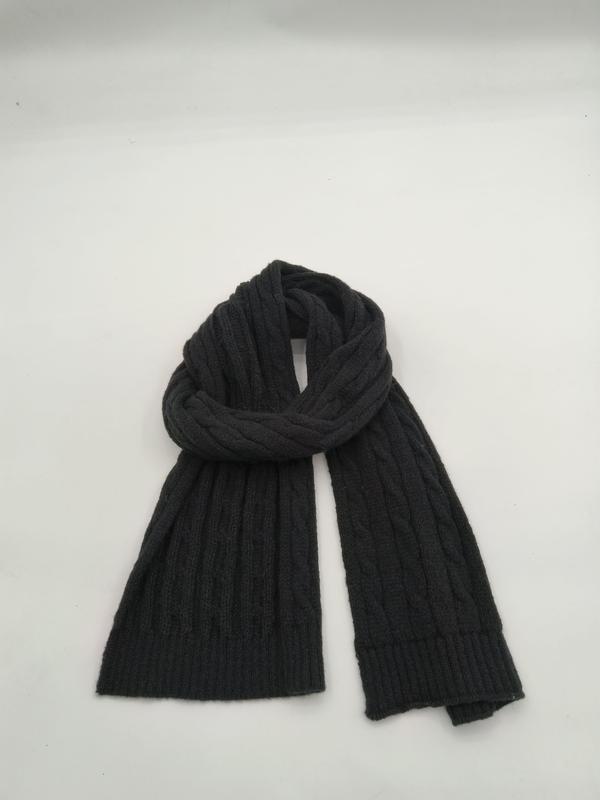 Dark charcoal grey cable knit scarf loosely coiled on white background, showing ribbed texture and two flat ends