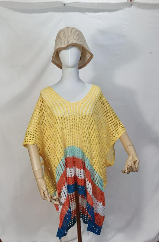 Mannequin wearing yellow crochet mesh poncho beach cover-up with multicolor stripes in teal, orange, white, blue at hem, paired with beige bucket hat
