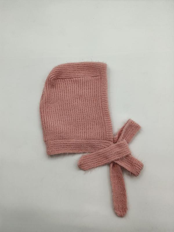 Soft pink ribbed knit baby bonnet with long tie strings laid flat on white background