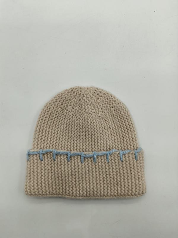 Beige chunky knit cuffed beanie hat with decorative light blue whipstitch detail along the folded brim, laid flat on white background