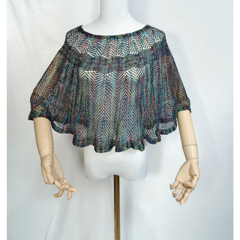 Multicolor open-weave knit crochet cape poncho displayed on mannequin with wooden articulated hands, bohemian mesh style