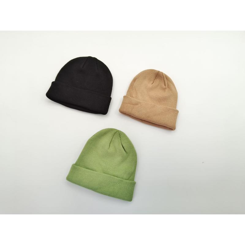 Three plain ribbed knit cuffed beanies laid flat in black, tan, and sage green on a white surface