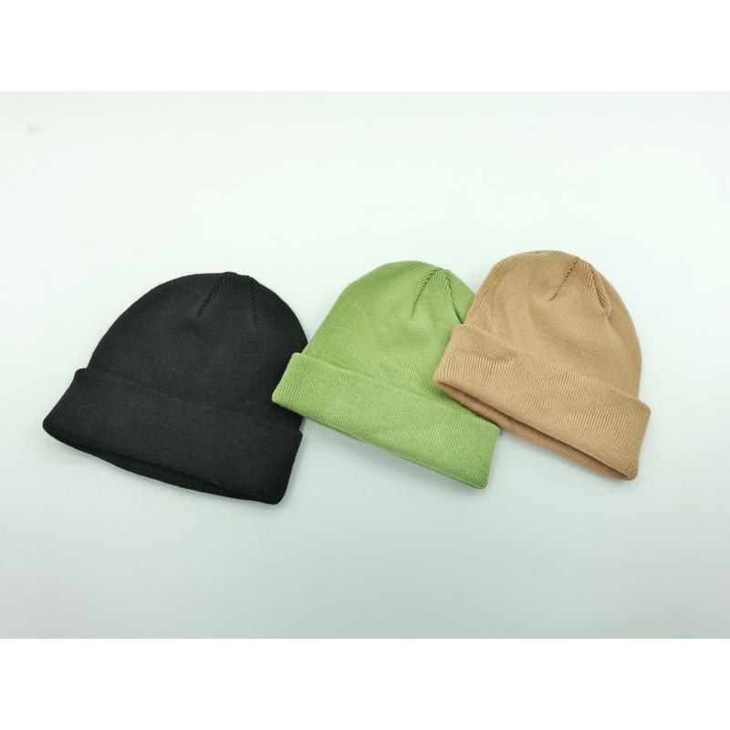 Three plain cuffed knit beanies laid flat in black, sage green, and tan on a white background