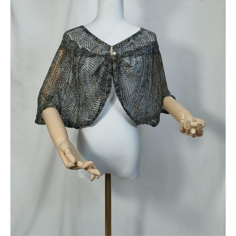 Blue gray metallic lace knit capelet shrug displayed on white mannequin with wooden hands, fastened with pearl brooch closure