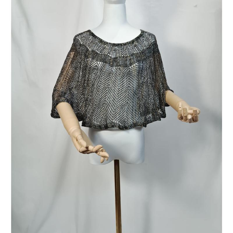 Cropped open-knit metallic silver and black cape poncho displayed on white mannequin with wooden articulated arms