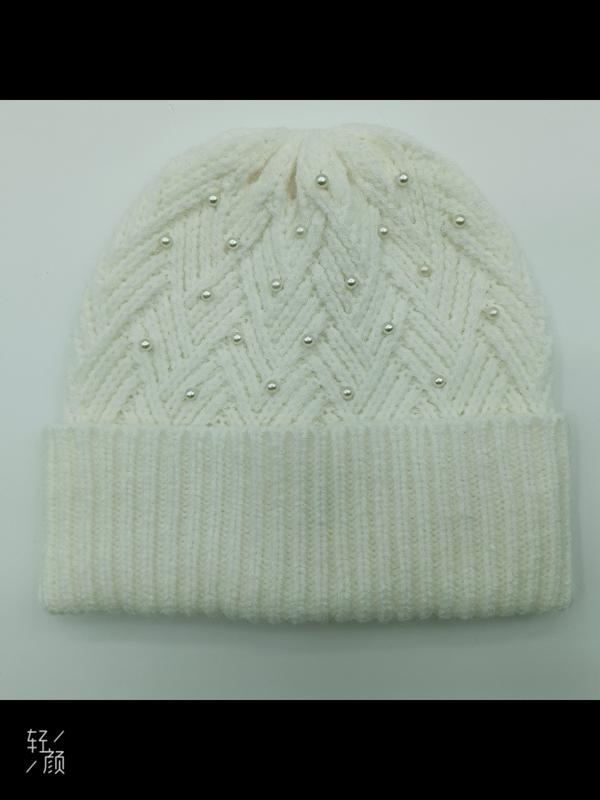 Cream white chunky knit winter beanie hat with herringbone pattern and scattered pearl bead decorations on flat surface