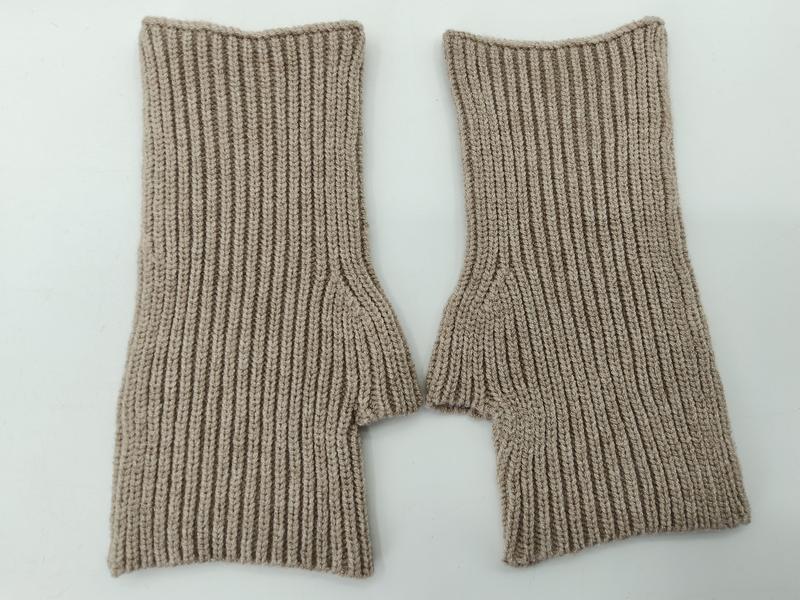 Pair of beige ribbed knit fingerless gloves laid flat on white background, showing thumb hole detail