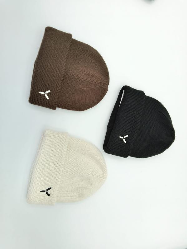 Three folded cuffed knit beanies in brown, black, and cream with small embroidered logo on white background
