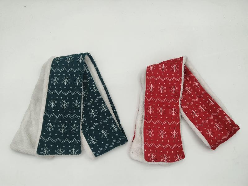 Two folded scarves with white snowflake fair isle pattern, teal and red with sherpa fleece lining, on white background