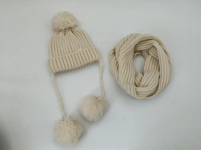 Cream ribbed knit winter beanie hat with pom-poms and braided ties alongside a matching infinity loop scarf set