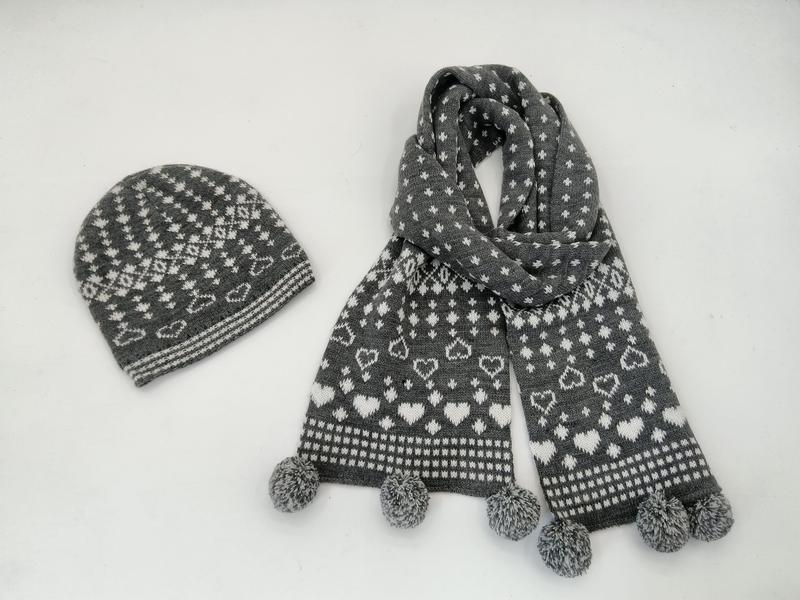 Grey and white Fair Isle knit beanie hat and scarf set with heart pattern and pom pom ends on white background