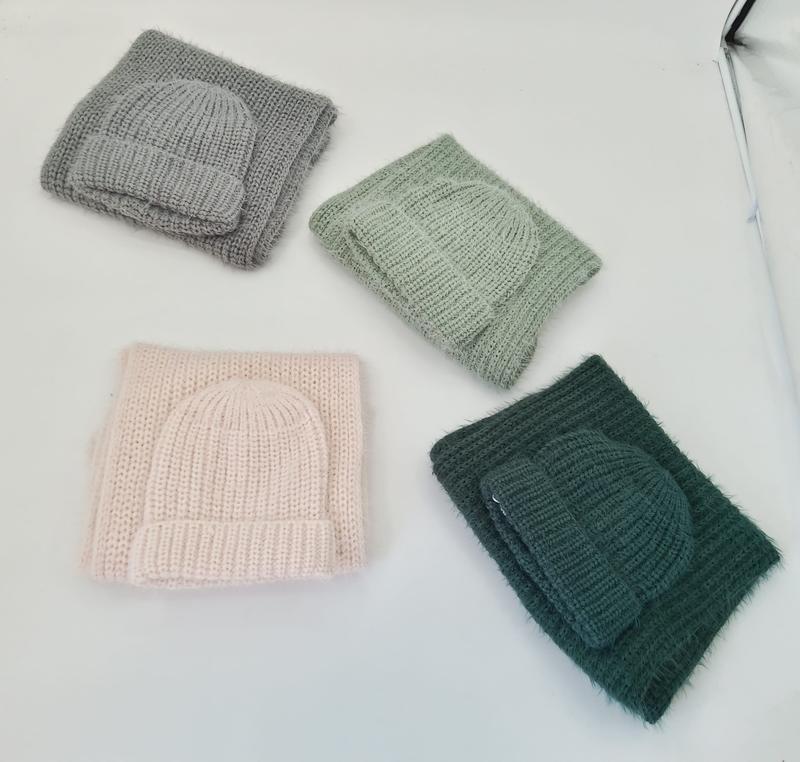 Four folded chunky knit winter hat and scarf sets in gray, sage green, blush pink, and dark forest green on white background